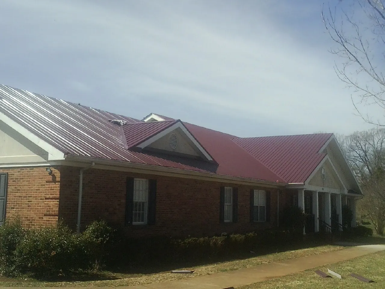 Red metal roof with gabled entries on a long brick building, from a Hail Damage Roof Repair job in Ringwood